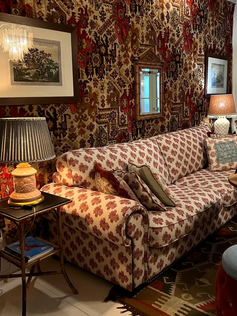 Salón con un sofá estampado en rojo, lámparas de mesa y tapices en las paredes