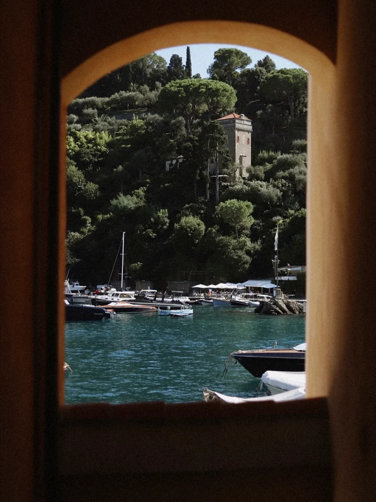 Ventana en arco que da a un puerto con barcos amarrados y una colina con árboles